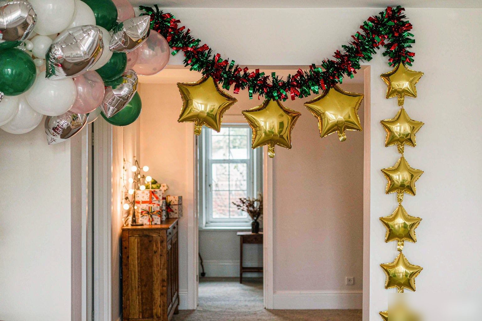 Red and green foil balloon garland above a doorway in a bright Christmas room