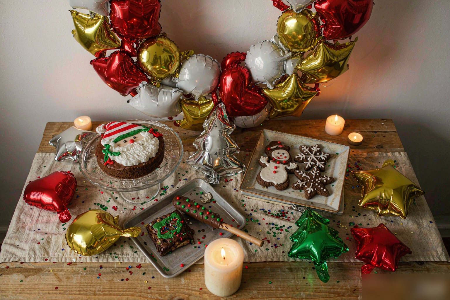 Christmas dessert and gift table with a foil balloon wreath behind it